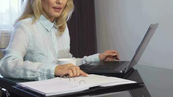 A woman reads important documents in a folder and types it into a laptop video