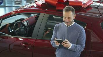 un sonriente hombre es en pie por el coche y mecanografía en el teléfono video