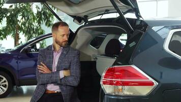 A young seller in a suit sits at the open trunk of the car video