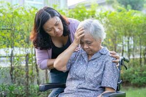 Asian elderly woman headache while sitting on wheelchair at park, healthy strong medical concept. photo