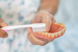 Asian elderly woman patient use toothbrush to clean partial denture of replacement teeth. photo