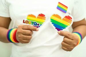 Asian lady wearing rainbow flag wristbands and hold heart, symbol of LGBT pride month celebrate annual in June social of gay, lesbian, bisexual, transgender, human rights. photo