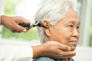 Audiologist or ENT doctor use otoscope checking ear of asian senior woman patient treating hearing loss problem. photo