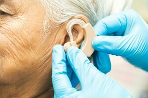 Asian senior woman patient wearing a hearing aid for treating hearing loss problem. photo