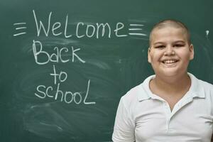 a boy standing in front of a blackboard with the words welcome back to school written on it photo