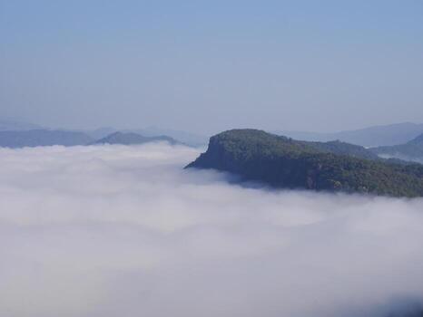 The mist flows through the mountain forest, Sun shining into tropical forest, Mist drifts through mountain ridges in the morning, slow floating fog blowing cover on the top of mountain photo