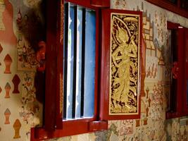 el de madera ventana es tallado en el imagen de un ángel participación un bandera. a wat phra singh chiang rai, hermosamente tallado rojo y dorado puerta a el wat phra singh templo en chiang rai, Tailandia foto