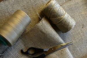 Yellow skeins of thread and scissors on a background of burlap. Yellow coarse cloth threads and scissors. photo