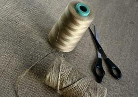 Yellow skeins of thread and scissors on a background of burlap. Yellow coarse cloth threads and scissors. photo