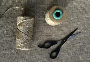 Yellow skeins of thread and scissors on a background of burlap. Yellow coarse cloth threads and scissors. photo