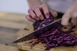 el cortar rojo repollo con un cocina cuchillo en un de madera corte tablero foto