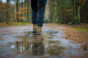 Selective focus shot of hiking boots walking through a puddle of water in the forest photo