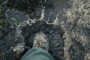 Hiking boot stepping into a puddle of muddy water photo