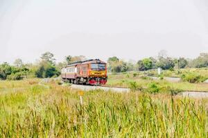 an orange train traveling through a grassy field photo