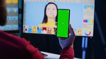 Photographer watching tutorial on mockup mobile phone to learn how to professionally enhance images quality. Photo editor following guide on green screen smartphone about using retouching software video