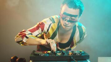 Young cool artist working as dj with turntables, mixing modern remix with bass and audio stereo equipment. DJ performer playing music with mixer and disc buttons. Handheld shot. photo