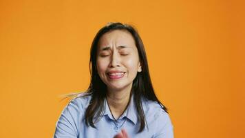 Filipino model praying for forgiveness and showing gratitude on camera, hopeful woman with belief in spirituality. Asian person with prayer hands having faith in God, orange background. video