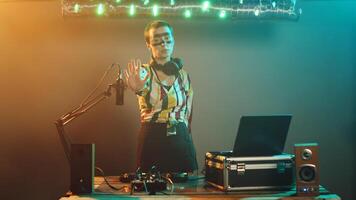 Crazy club musician raising palm to show denial and stop symbol on stage, mixing modern techno sounds on DJ turntables. Performer using audio stereo instruments, adjusting buttons. Tripod shot. photo