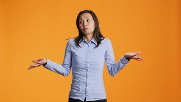 Doubtful model raising shoulders over orange background, showing doubt and being clueless about answer. Young filipino person acting uncertain and confused standing in front of camera. video