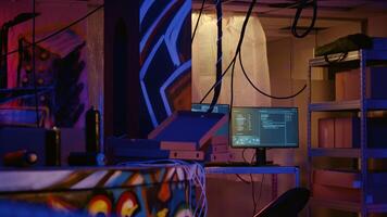 Zoom in on advanced technology computers left open running code in empty neon lit basement with graffiti drawings painted on walls. High tech equipment used by hackers in underground warehouse photo