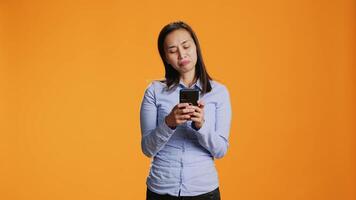 Young person texting messages on mobile device in studio, browsing through social media app and talking to friends online. Modern smiling woman using sms and texts for communication. video