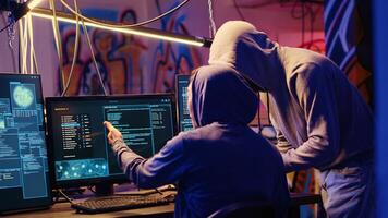 Evil cybercriminals in graffiti sprayed hideaway targeting vulnerable unpatched connections, discussing ways of getting past computer defenses and stealing valuable sensitive data photo