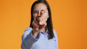 During the shot, pleased filipino girl points index finger at the lens. Confident young woman with calm mood using charm and personality, standing over orange background illustrating stuff. video