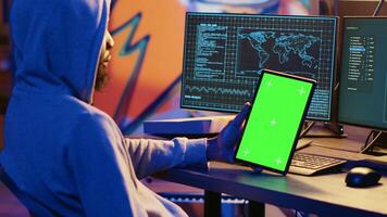 Hacker using VPN as anonymity tool to mask his online identity while committing data breaches using green screen tablet. Cybercriminal in bunker masking his location, hacking with mockup device photo
