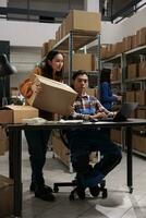 Storehouse package carrier giving parcel to delivery manager in post office storage room. Postal service warehouse asian employees team coordinating cardboard box shipment photo