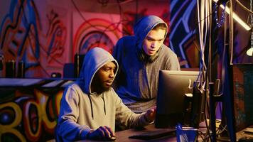 New member in hacking group receiving guidance from knowledgeable rogue programmer acting as his mentor in hidden base. African american hacker teaches script kiddie how to hack computers photo