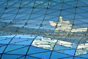 Glass building with transparent facade of the building and blue sky. Structural glass wall reflecting blue sky. Abstract modern architecture fragment. Contemporary architectural background. photo