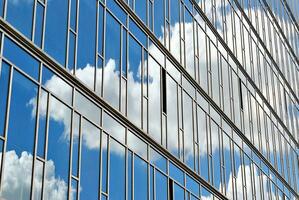 Glass building with transparent facade of the building and blue sky. Structural glass wall reflecting blue sky. Abstract modern architecture fragment. Contemporary architectural background. photo