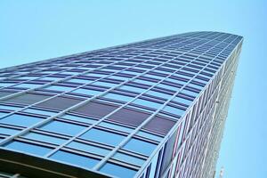 Glass building with transparent facade of the building and blue sky. Structural glass wall reflecting blue sky. Abstract modern architecture fragment. Contemporary architectural background. photo