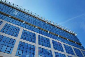 Glass building with transparent facade of the building and blue sky. Structural glass wall reflecting blue sky. Abstract modern architecture fragment. Contemporary architectural background. photo