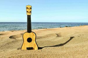 a wooden ukulele sits on the sand near the ocean photo