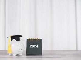 Study goals, 2024 Desk calendar and Piggy bank with graduation hat. The concept of saving money for education, student loan, scholarship, tuition fees in New Year 2024 photo