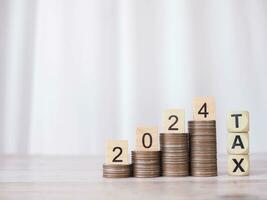 Wooden block with number 2024 on stack of coins and Wooden blocks with the word TAX. The concept of saving money for payment tax, Financial, Investment and Business growing in new year 2024. photo