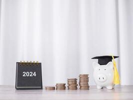 Study goals, 2024 Desk calendar, Piggy bank with graduation hat and stack of coins. The concept of saving money for education, student loan, scholarship, tuition fees in New Year 2024 photo