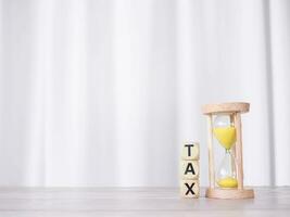 Hourglass and wooden blocks with the word TAX on stack of coins. The concept for manage time to paying tax photo