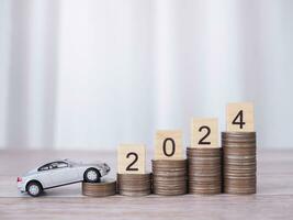 Wooden black with number 2024 on stack of coins and toy car. The concept of saving money for car loan, insurance, paying tax in new year 2024 photo