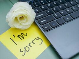 Top view of words i'm sorry written on sticky note on laptop keyboard with roses photo