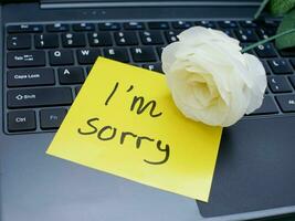 Top view of words i'm sorry written on sticky note on laptop keyboard with roses photo