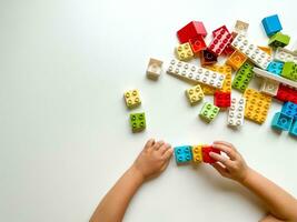 Child playing with colorful building blocks on white background. Top view photo