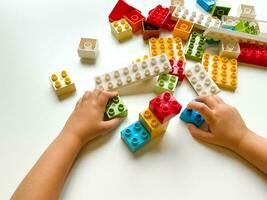 Child playing with colorful building blocks on white background. Top view photo