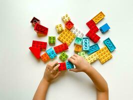 Child playing with colorful building blocks on a white background. Top view photo