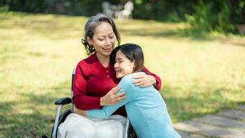 Asian senior woman in wheelchair with happy daughter. Family relationship retired woman sitting on wheelchair in the park age care at retirement home. photo