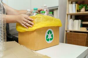 Home recycle eco green zero concept Woman throwing empty plastic bottle in recycling bin with yellow garbage bags at home. photo