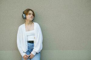 Portrait of a teenage girl in headphones against a gray wall. photo