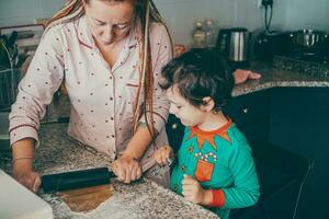 fiesta magia viene viva en el cocina como un alegre mamá y su hijo preparar Navidad pan de jengibre foto