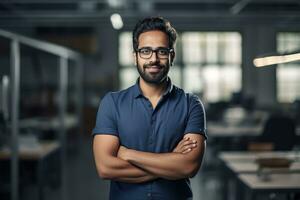 ai generado un joven indio masculino diseñador, ingeniero, arquitecto quien es vistiendo lentes y un azul camisa sonriente en pie en el oficina y mirando a el cámara foto